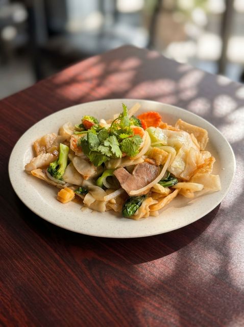 Plate of sliced meat and vegetables topped with cilantro on a dark wooden table in sunlight