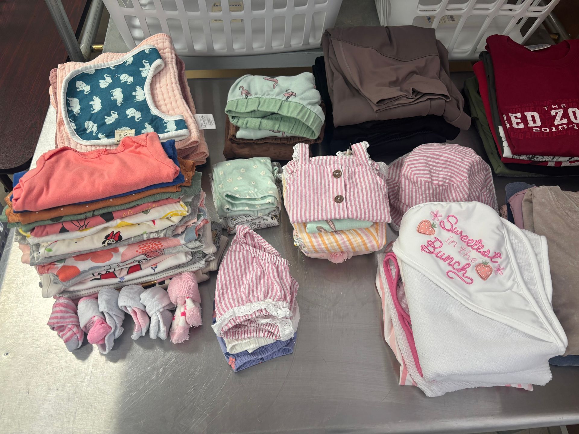 Baby clothes stacked on a table: shirts, hats, bibs, and socks in various colors.