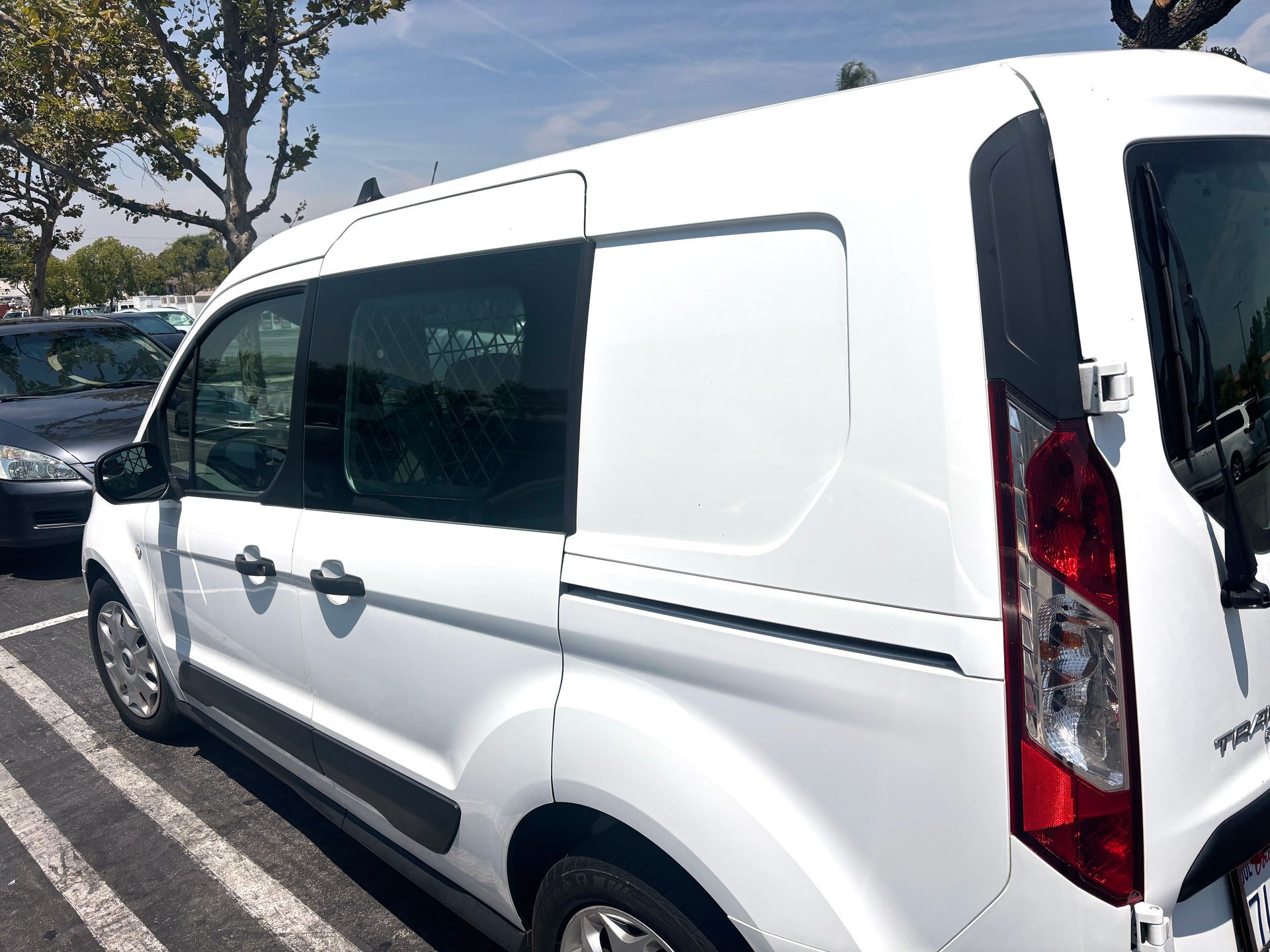 White cargo van parked in a lot, seen from the side. The van is against a blue sky, with trees in the background for delivery use. 