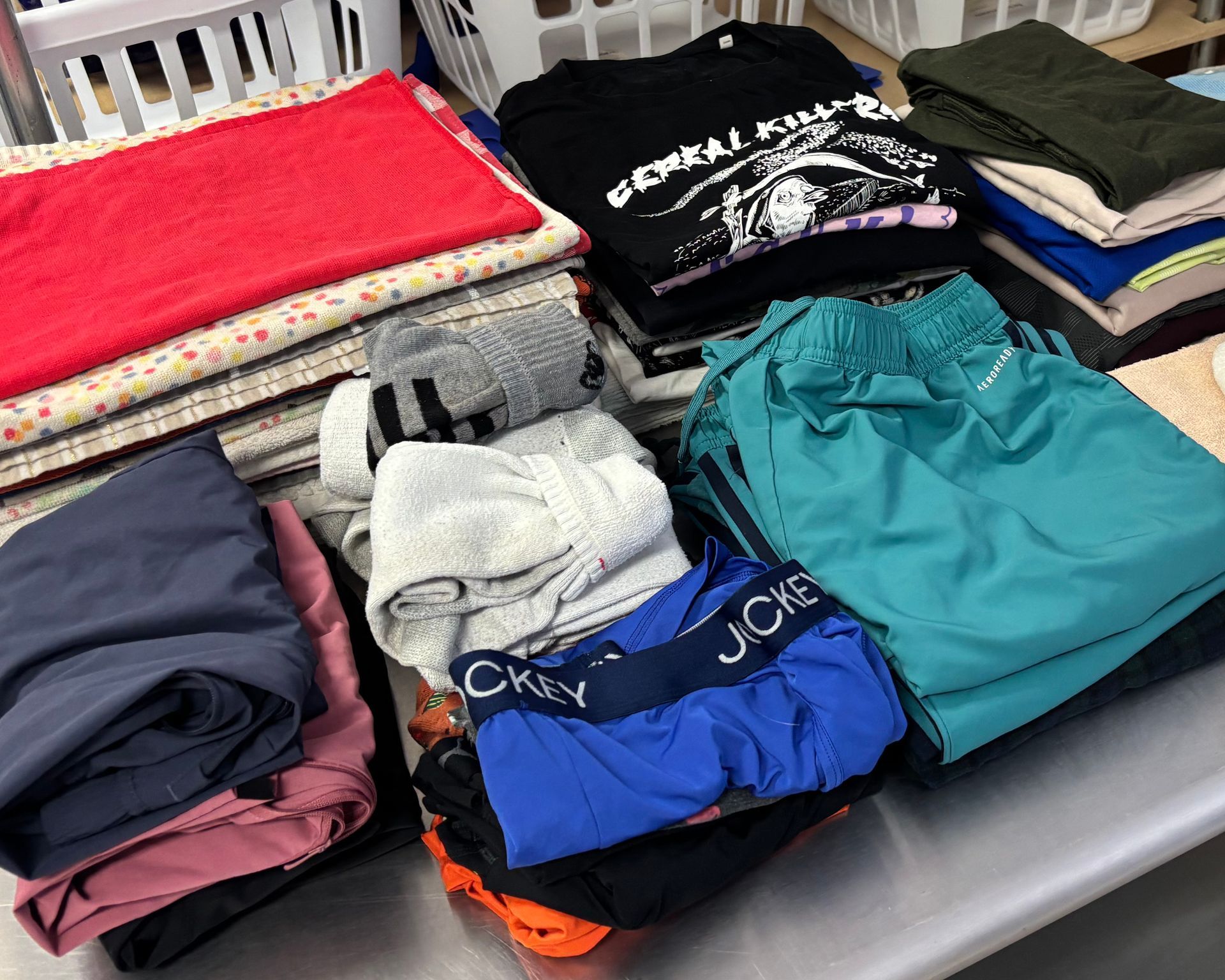 A stack of folded laundry, including shirts, shorts, and towels in various colors, on a metal surface.