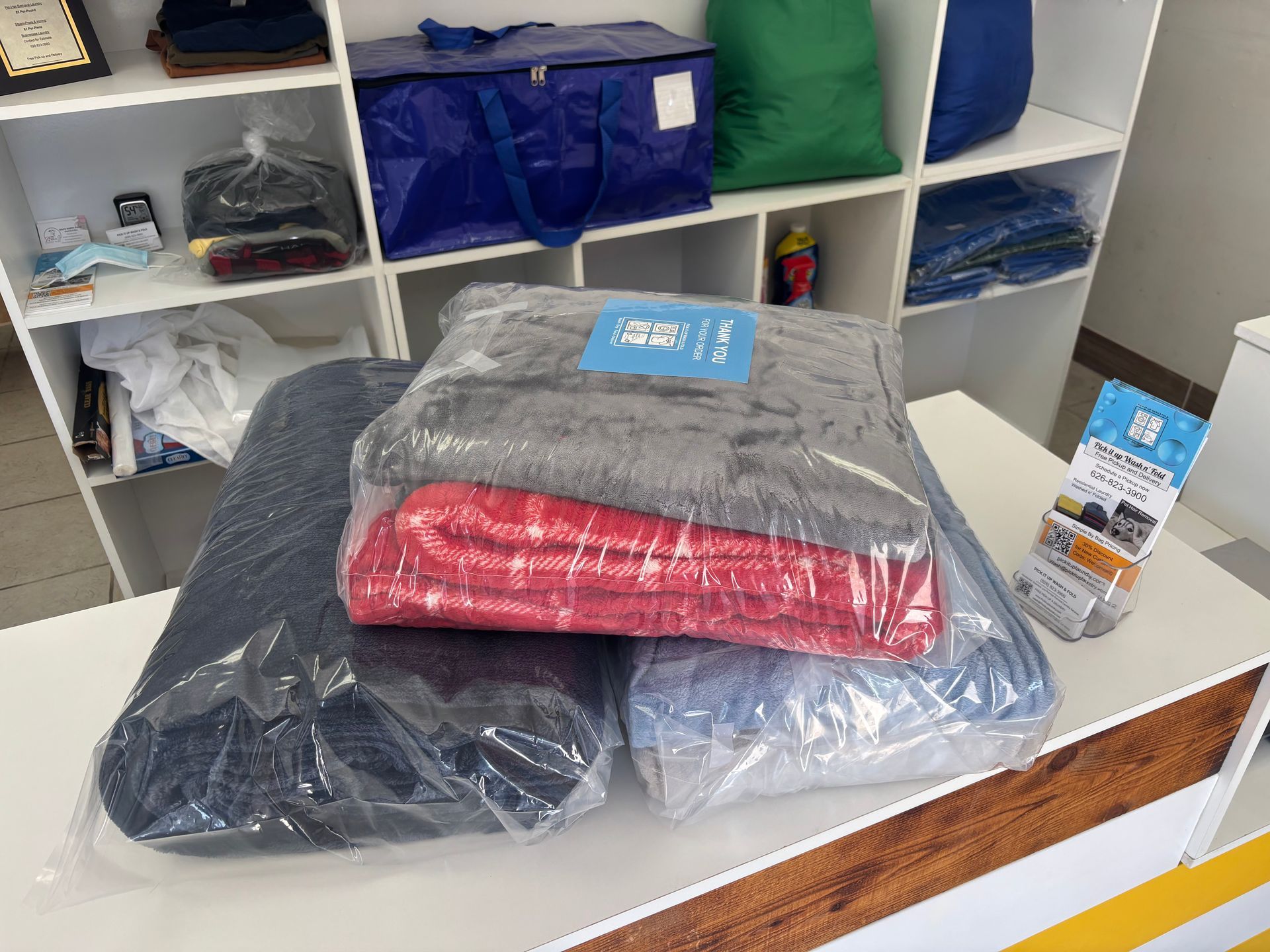 Wrapped blankets on a table, shelves with storage bags in background.
