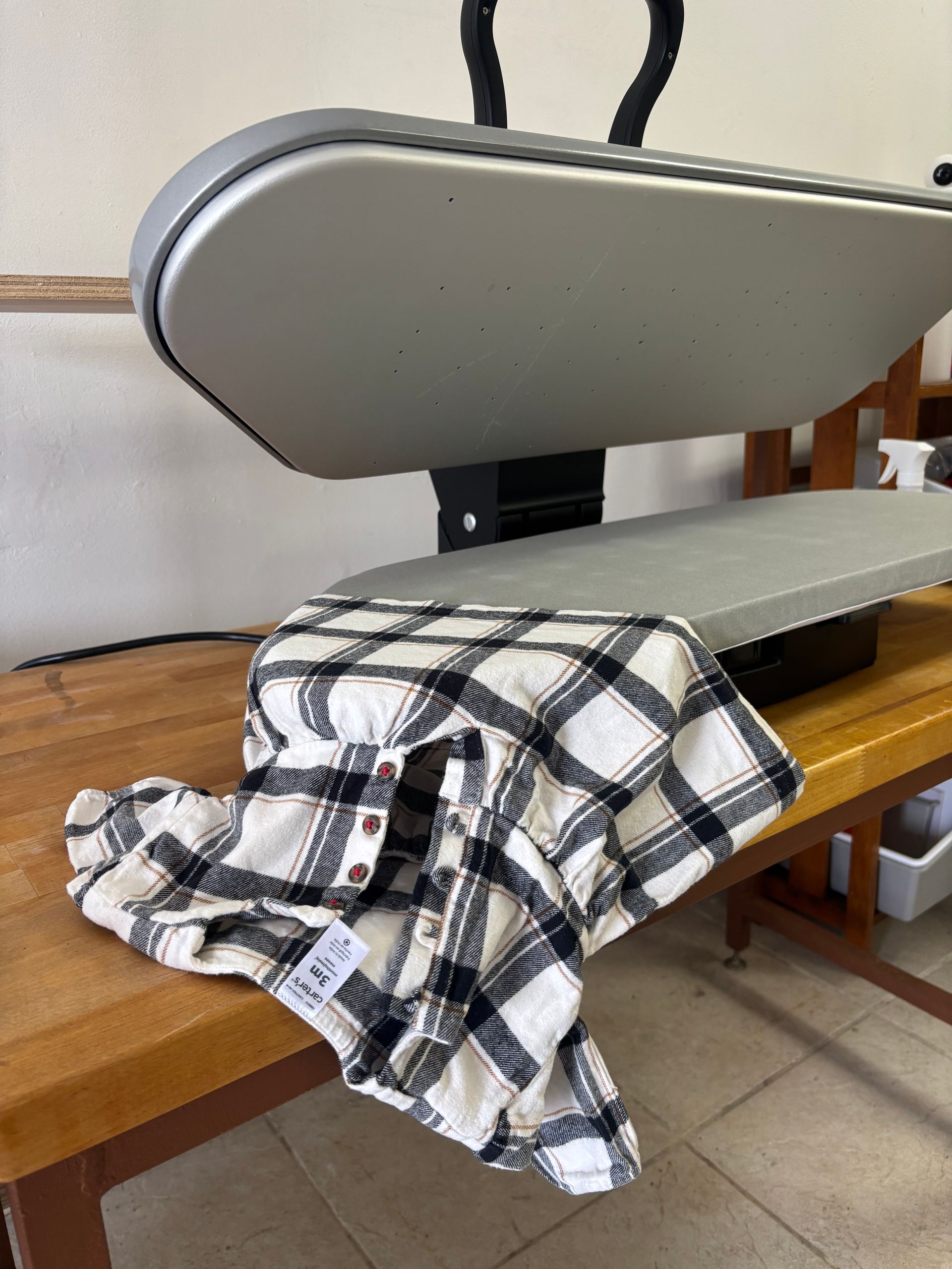 Plaid shirt on a wooden table under a large, gray heat press.