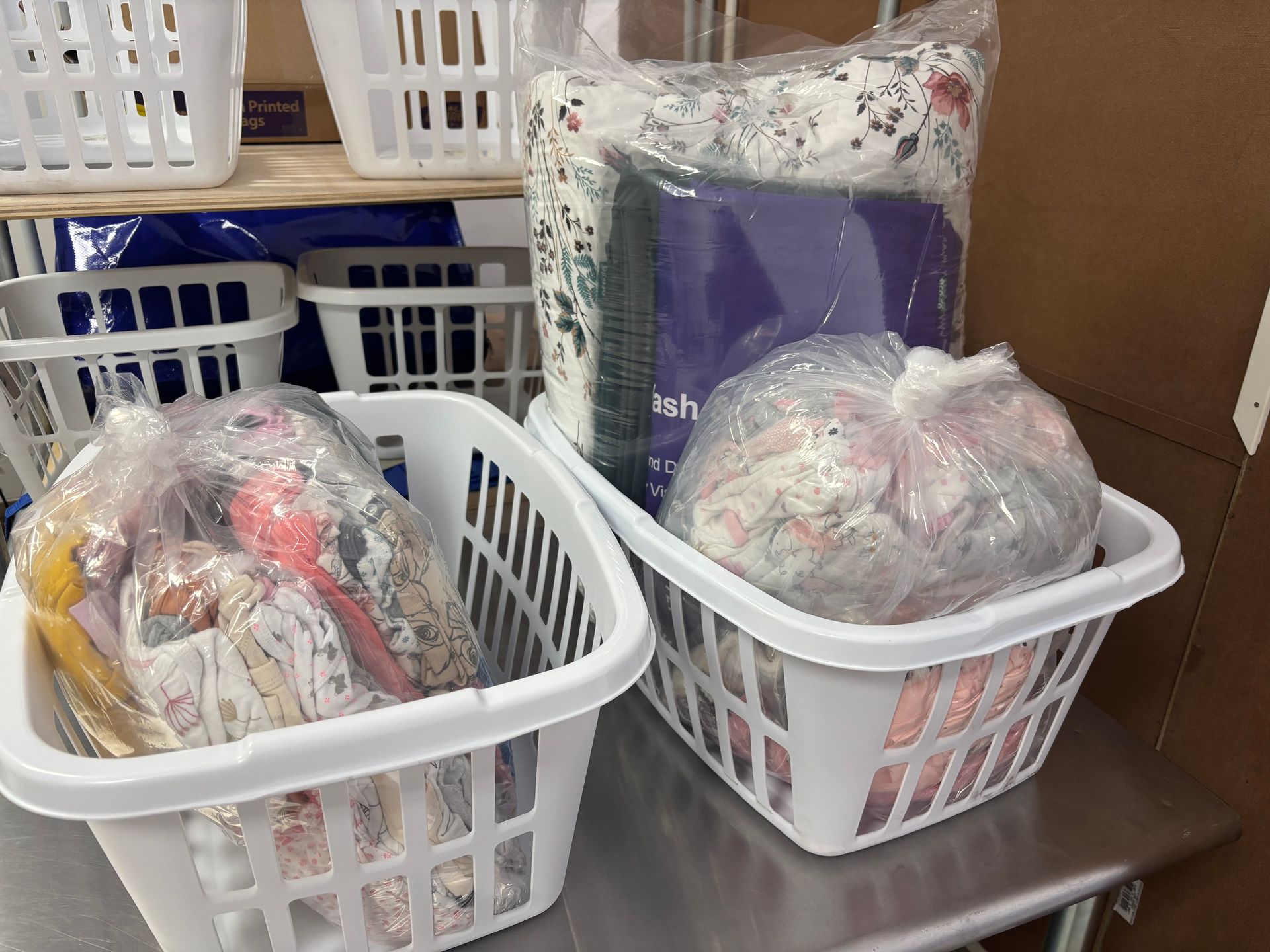 White laundry baskets filled with bagged textiles, shelves, and a stainless steel surface.