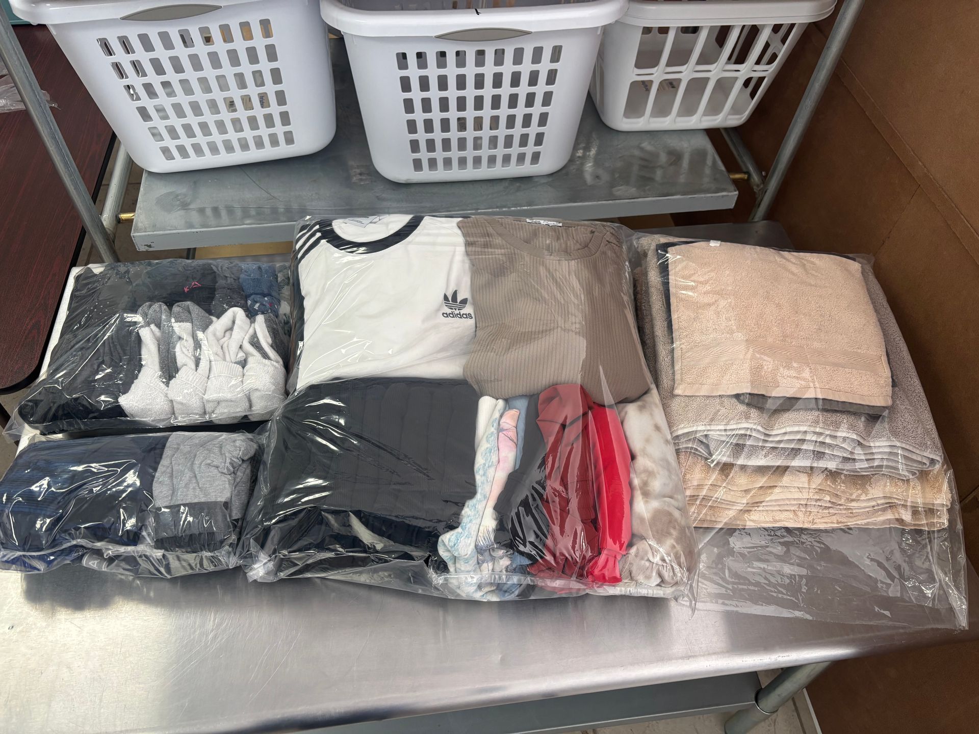 Laundry baskets above neatly bagged and folded clothing on a stainless steel table.