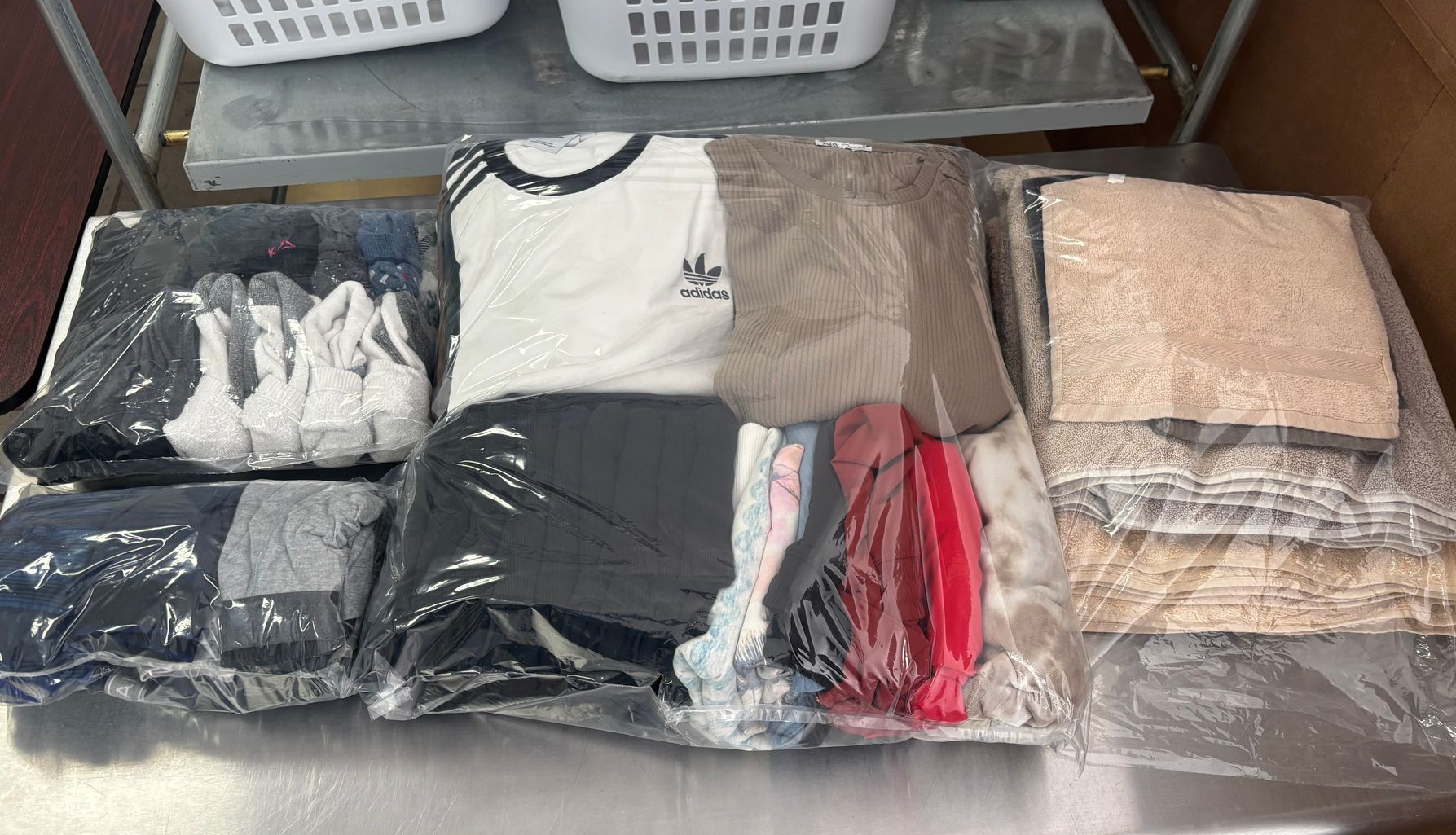 Laundry baskets above neatly bagged and folded clothing on a stainless steel table.