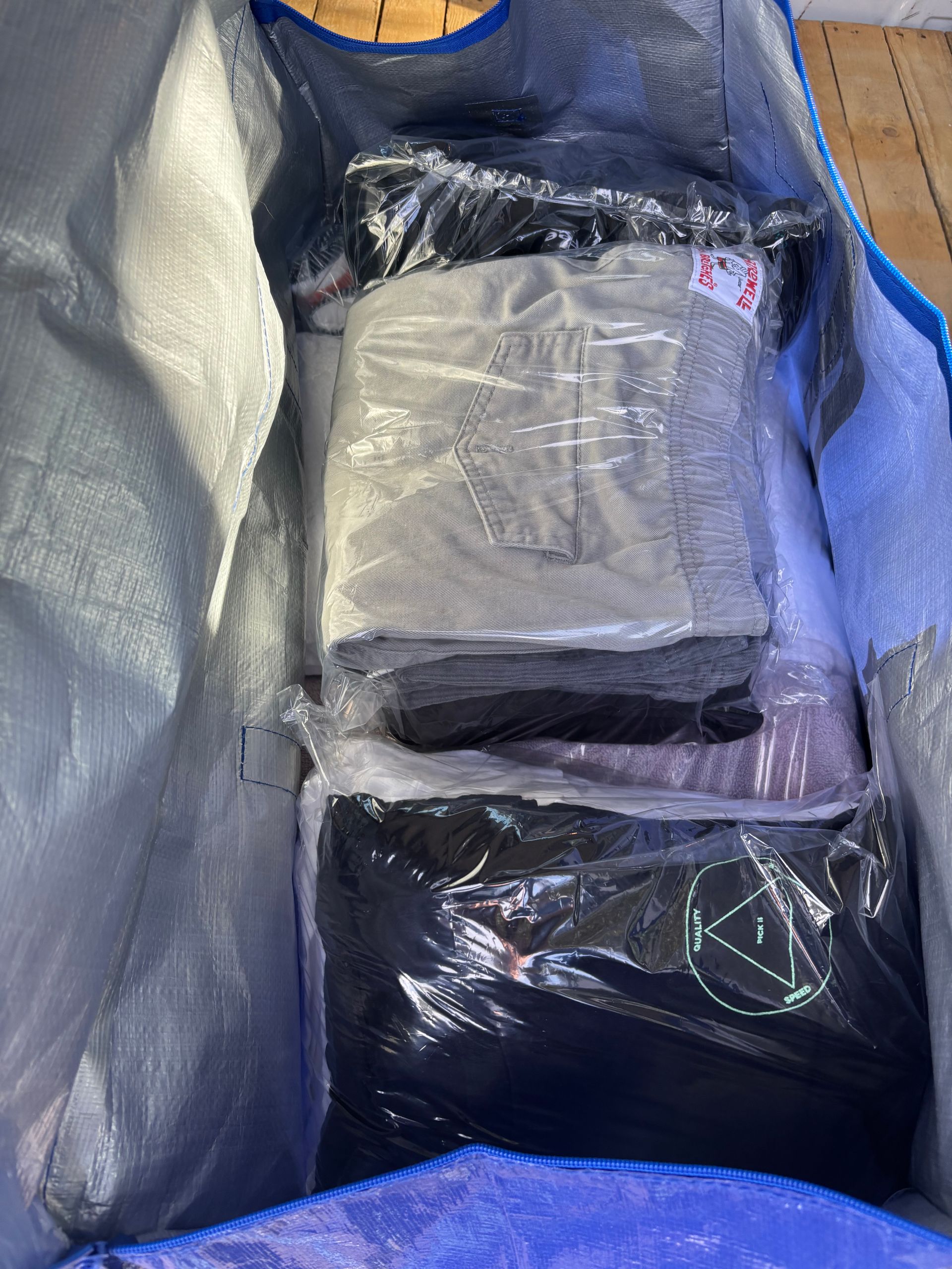 Blue bag filled with several bundled clothing items wrapped in plastic.