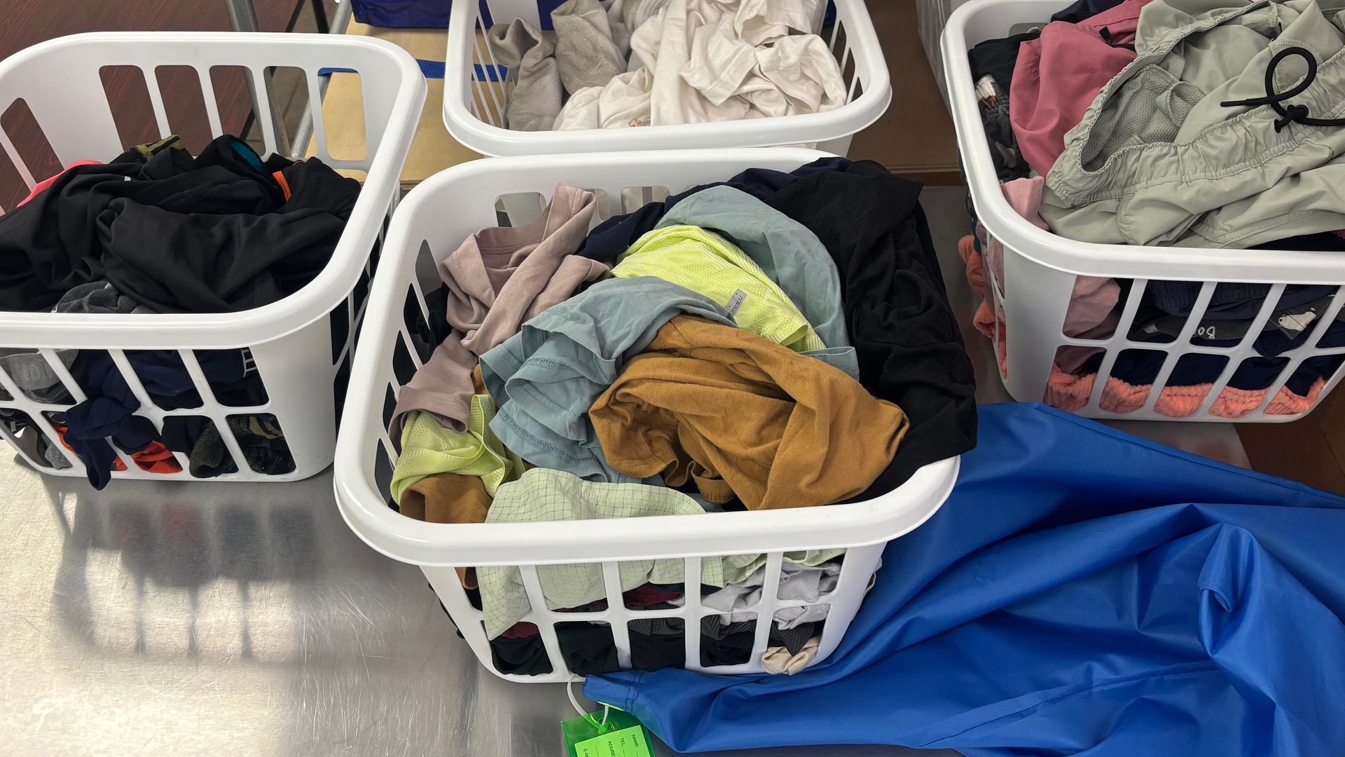 Laundry baskets filled with colorful clothes sit on a metal surface.