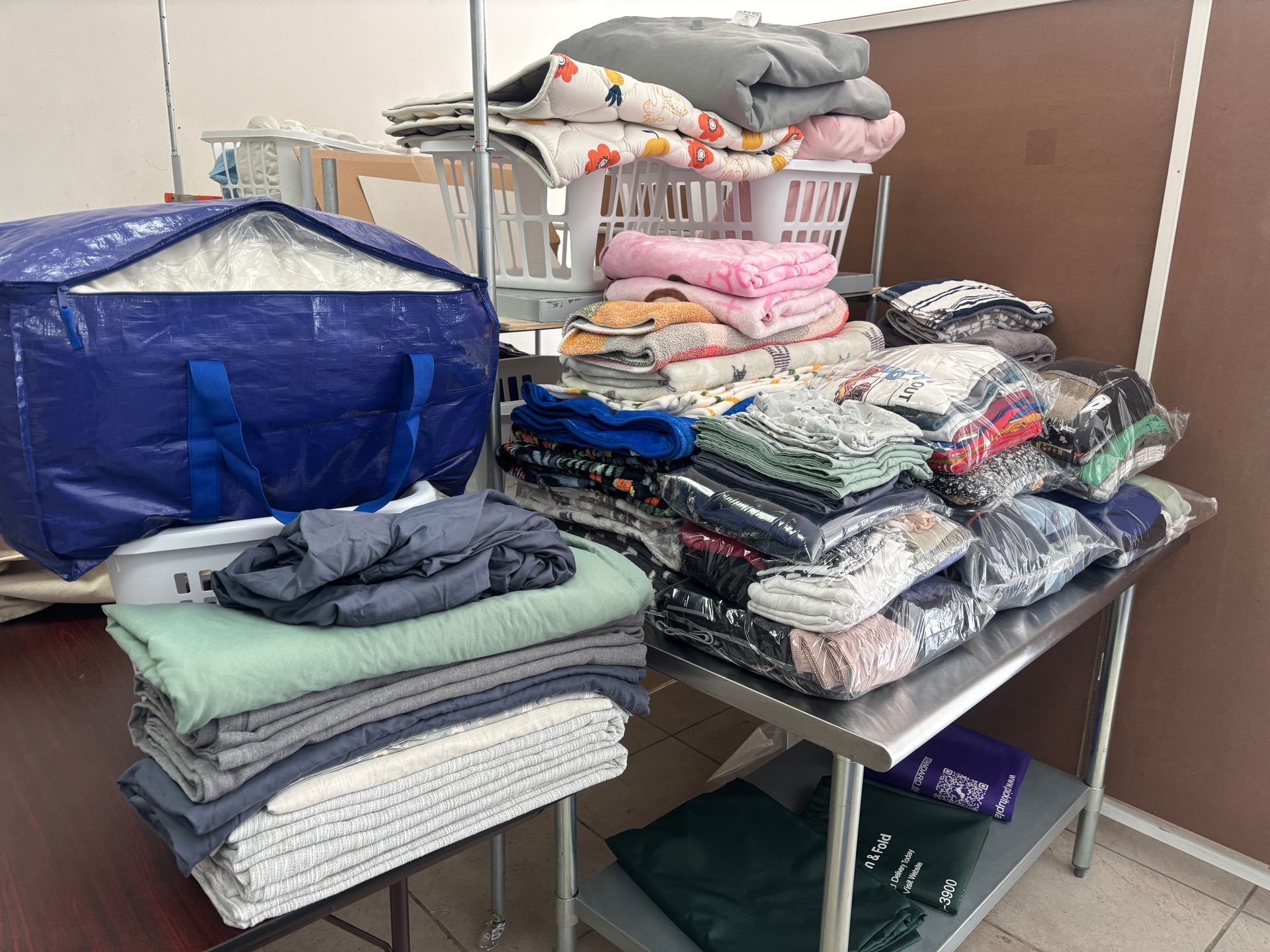 Two folded blankets, one gray and one blue, wrapped in plastic on a silver surface.