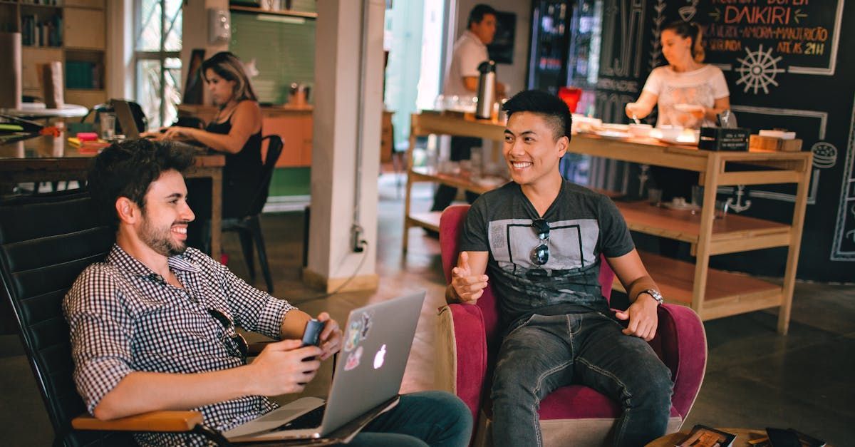 Two men are sitting in chairs with laptops in a restaurant.