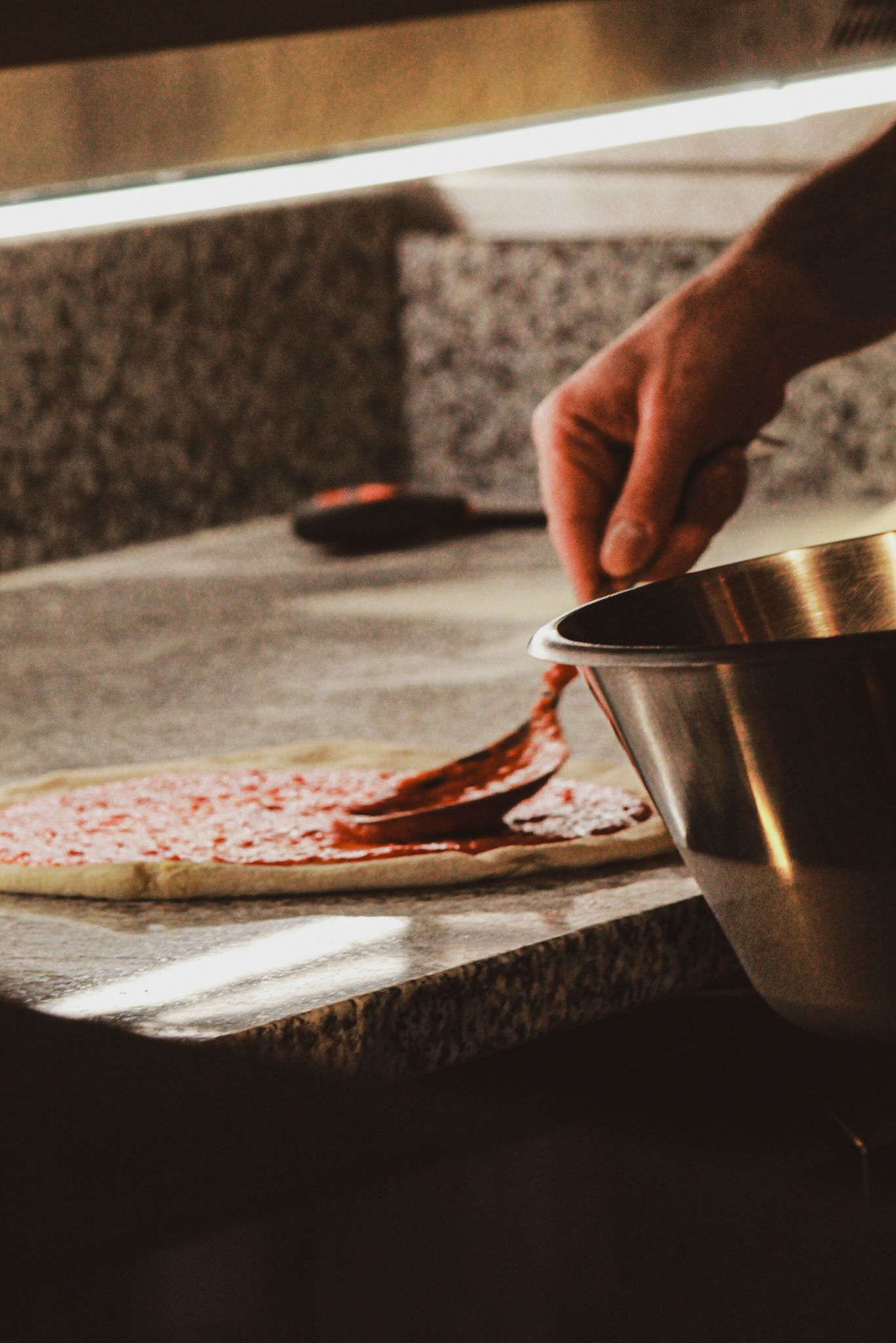Una persona sta spalmando la salsa su una pizza con un cucchiaio.