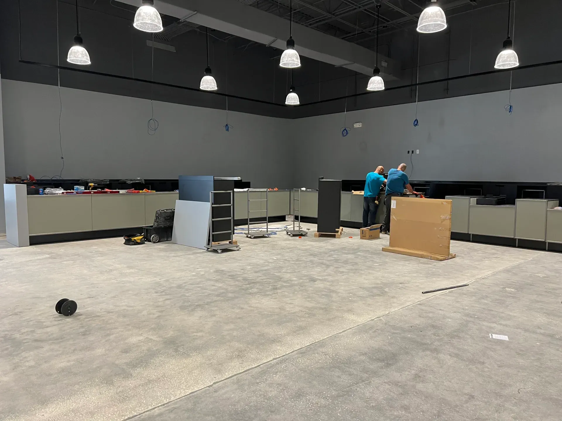 Interior of a commercial space under construction. Workers installing cabinets along a gray wall.