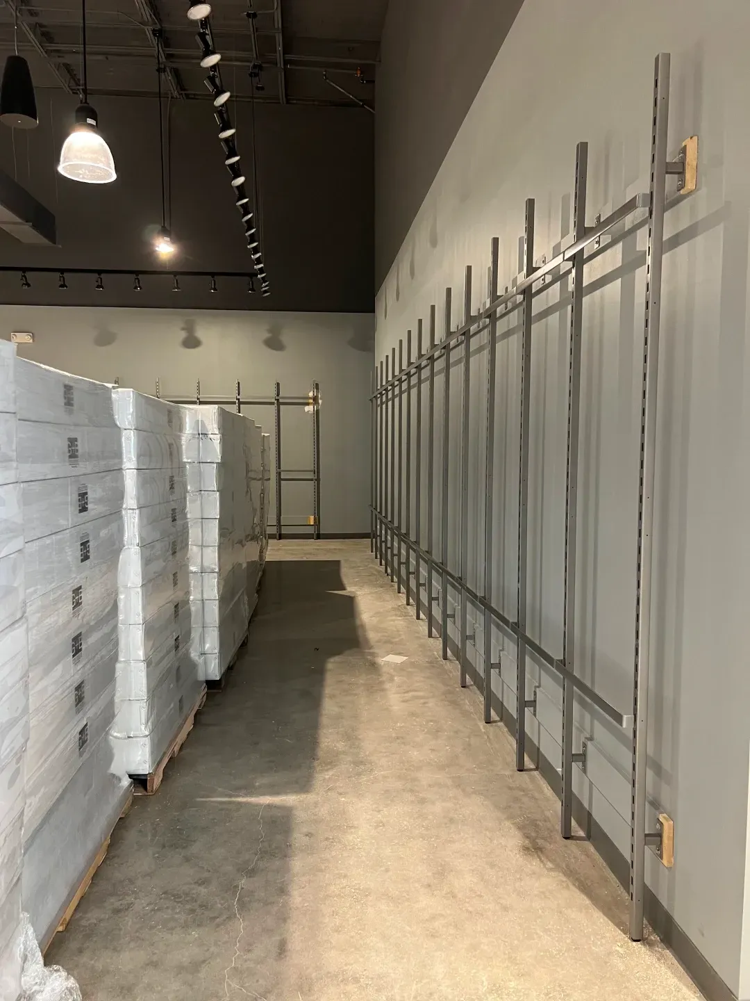 Empty retail space; grey walls, unfinished displays. Pallets of boxes on the left.
