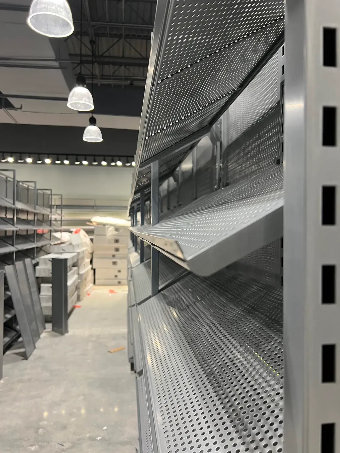 Metal shelving in a store, partially constructed with holes in the surfaces, and empty.