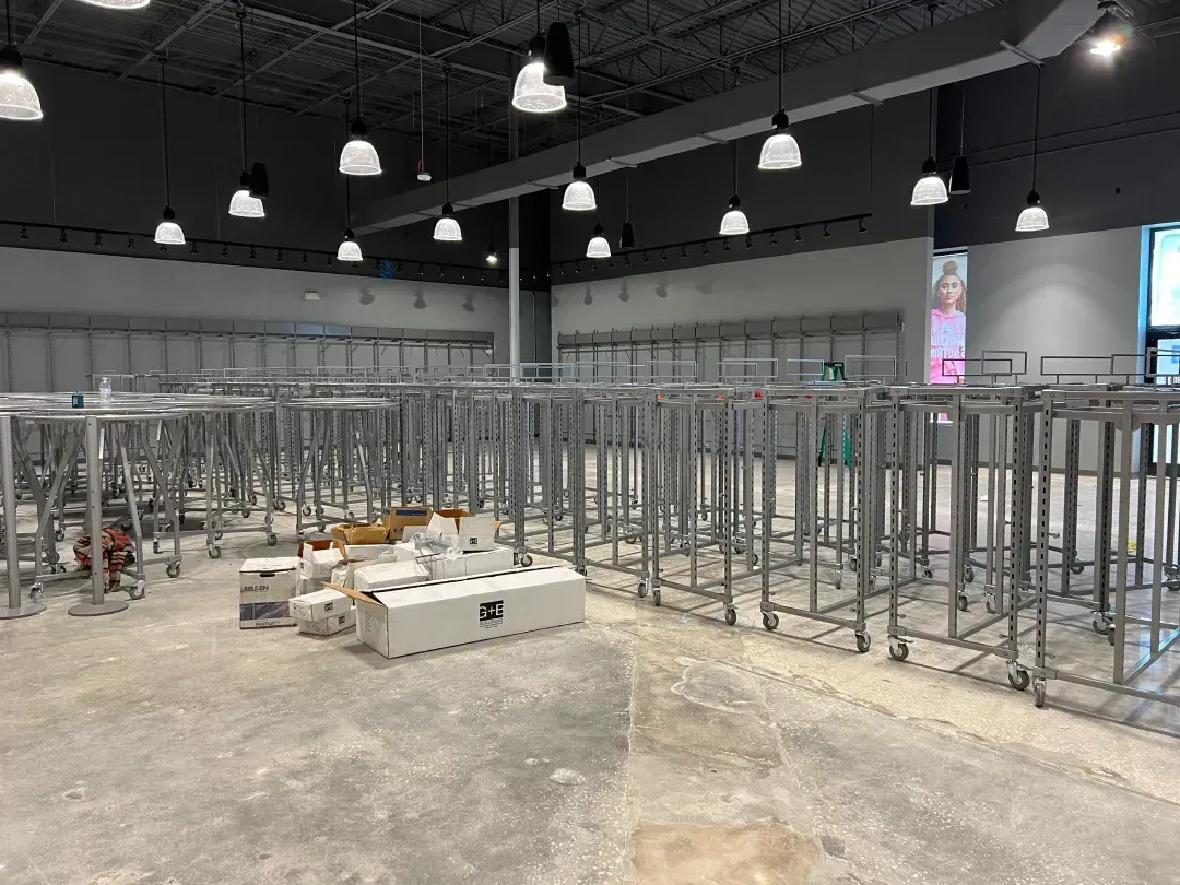 Empty retail store interior with metal clothing racks, gray floors, and ceiling lights.