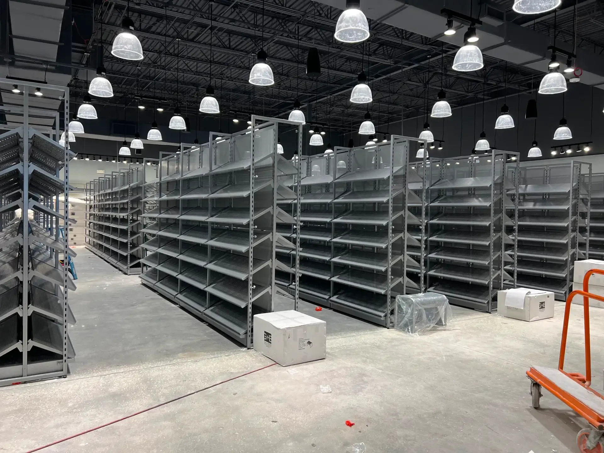 Rows of empty metal shelves in a large, bright warehouse-like space, with overhead lights.