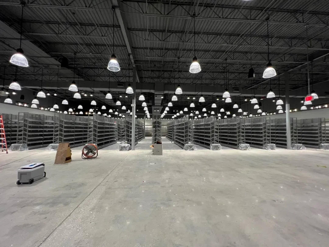 Empty warehouse interior with rows of metal shelving and overhead lights. Construction in progress.