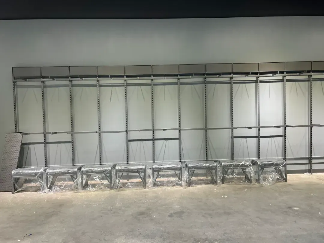 Metal frame structure with rows of shelves, against a gray wall and floor.