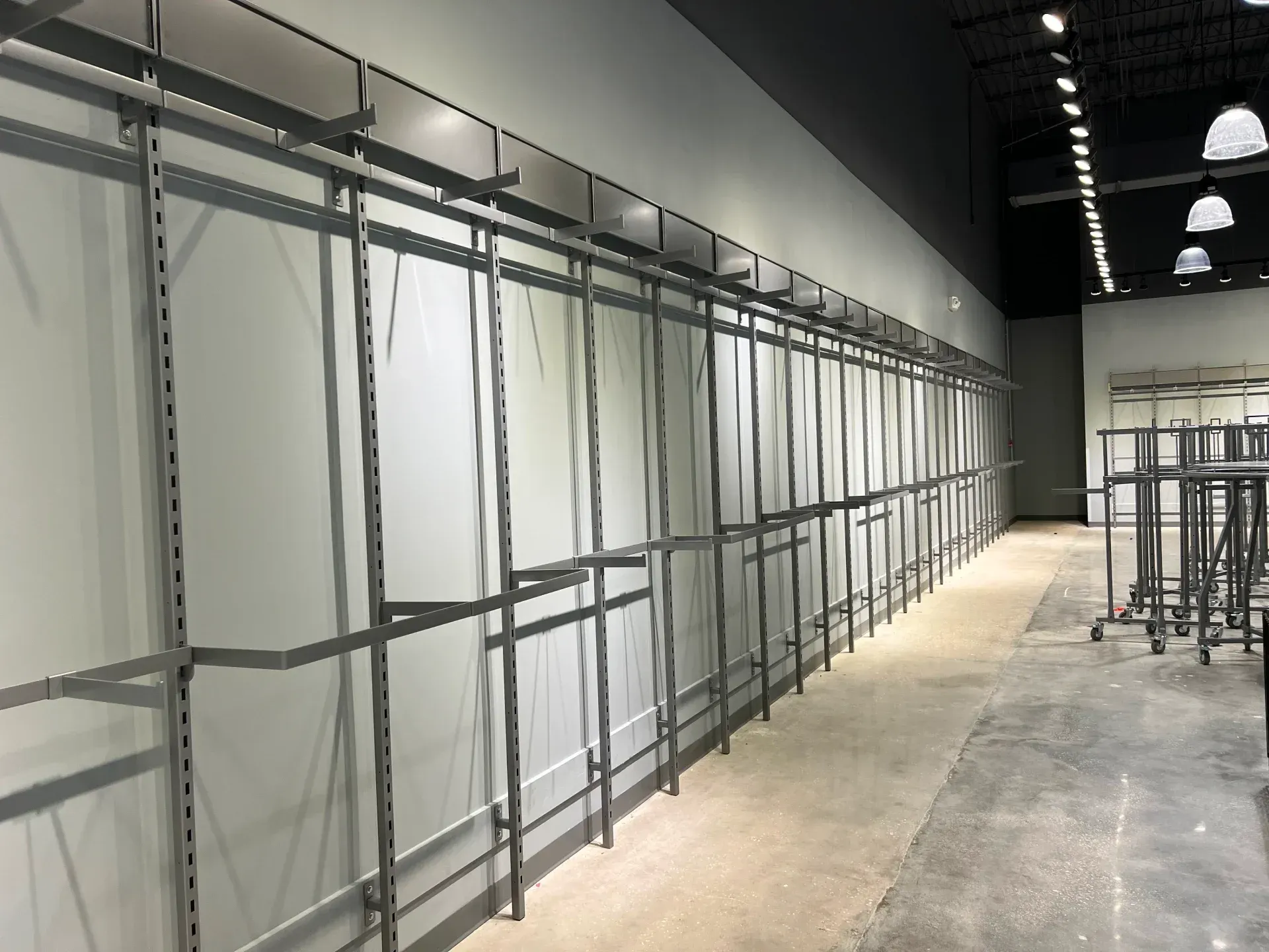 Empty retail space with metal shelving along a white wall and a dark ceiling.