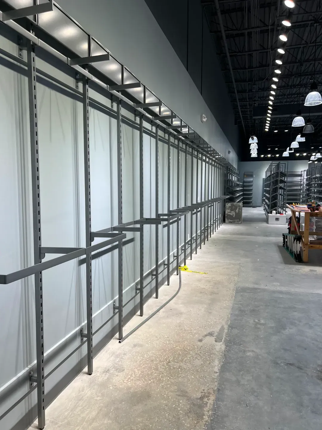 Empty retail space with metal shelving along a white wall and concrete floor.
