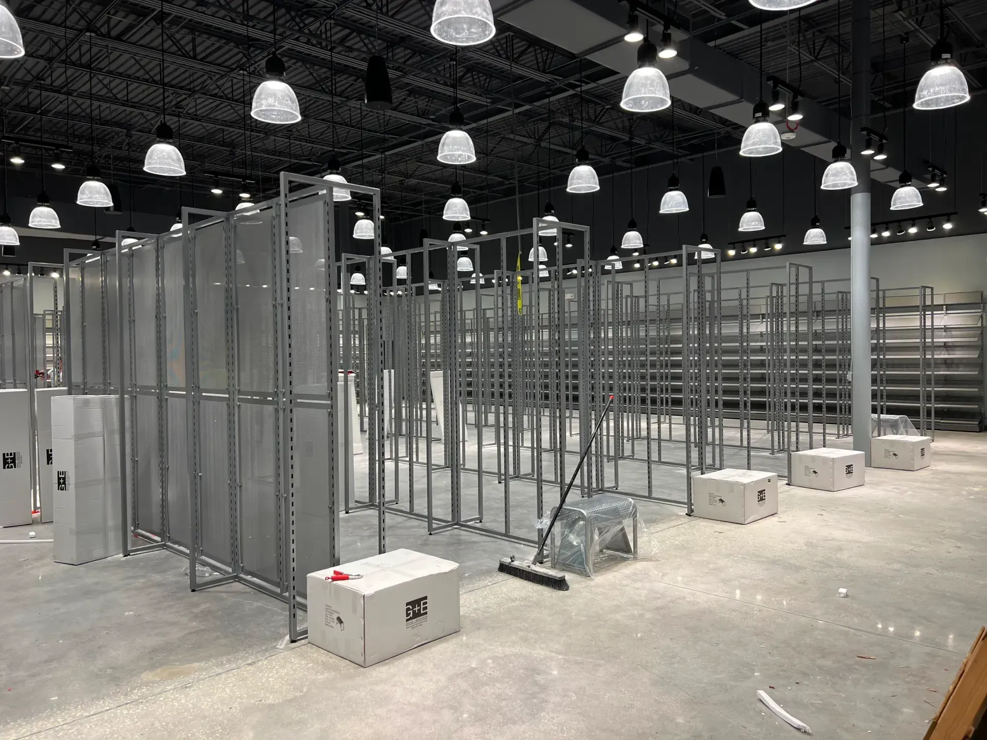 Empty retail store interior, metal shelving structures, unfinished floor, overhead lights.
