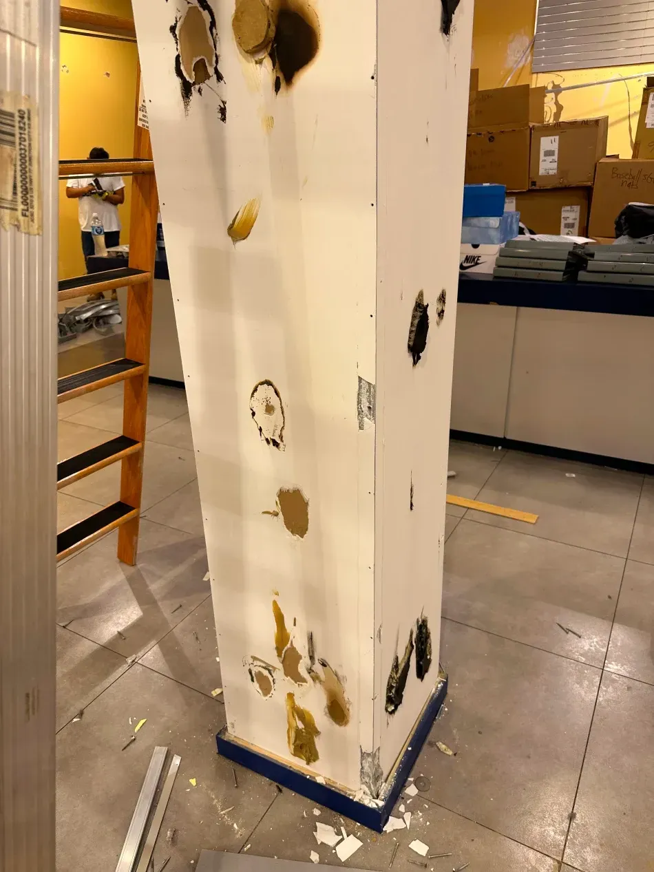 Damaged white column with brown and black marks. A person on a ladder is visible in the background.