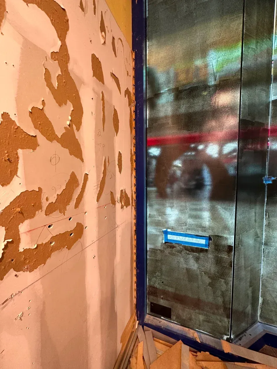 Peeling paint on a wall next to a window with blue tape.