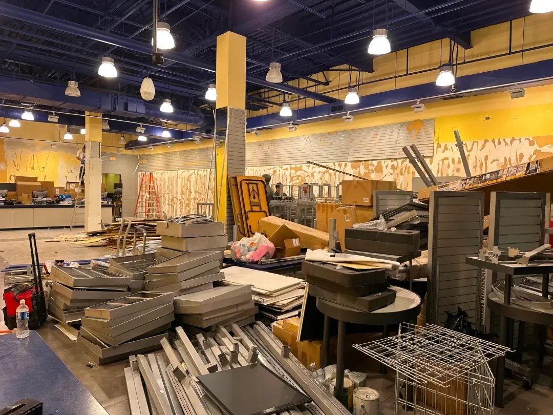 Interior of a store in disarray during renovation; debris, boxes, and dismantled shelving scattered about.