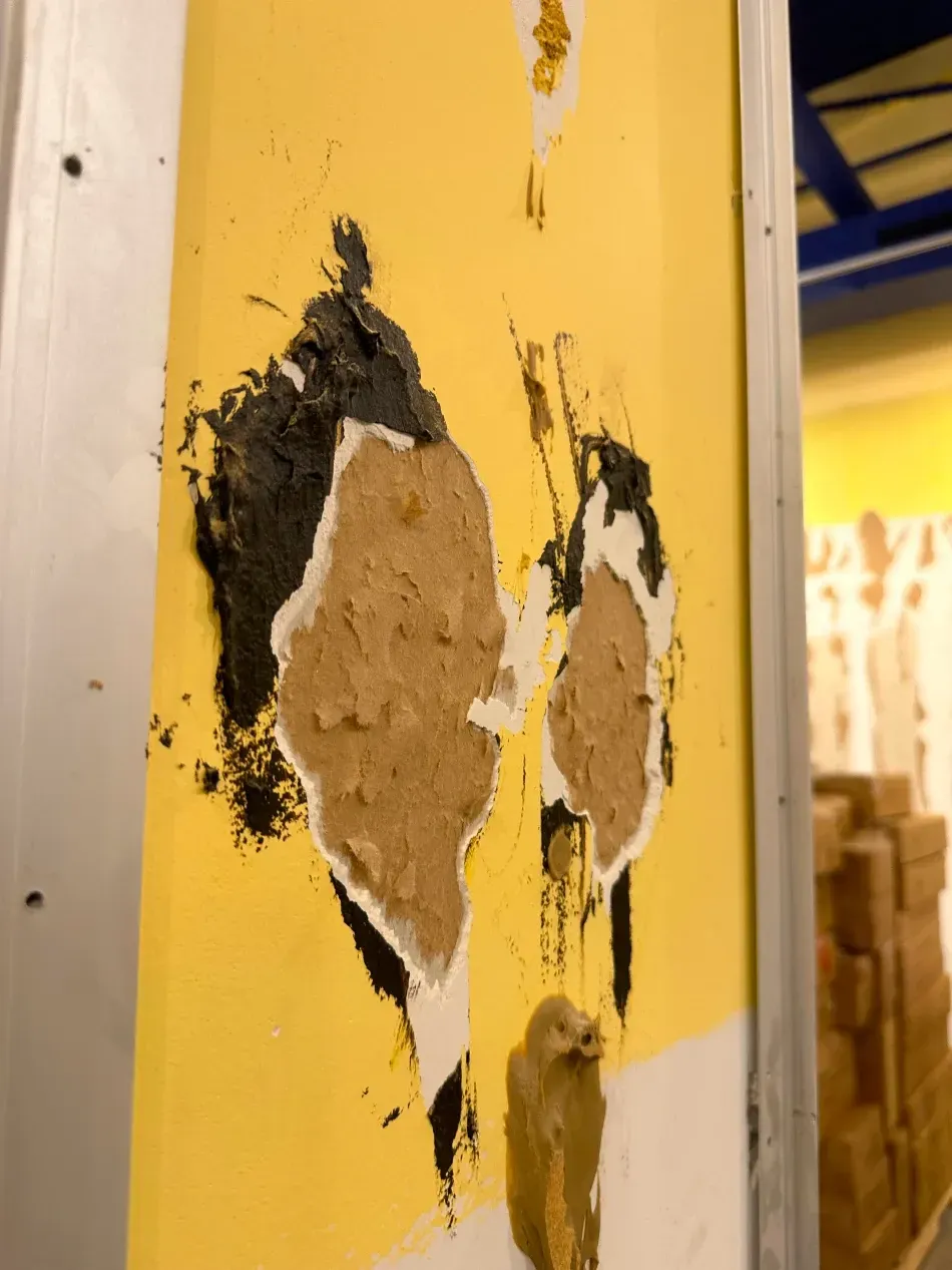 Damaged yellow wall with exposed brown material and black residue.