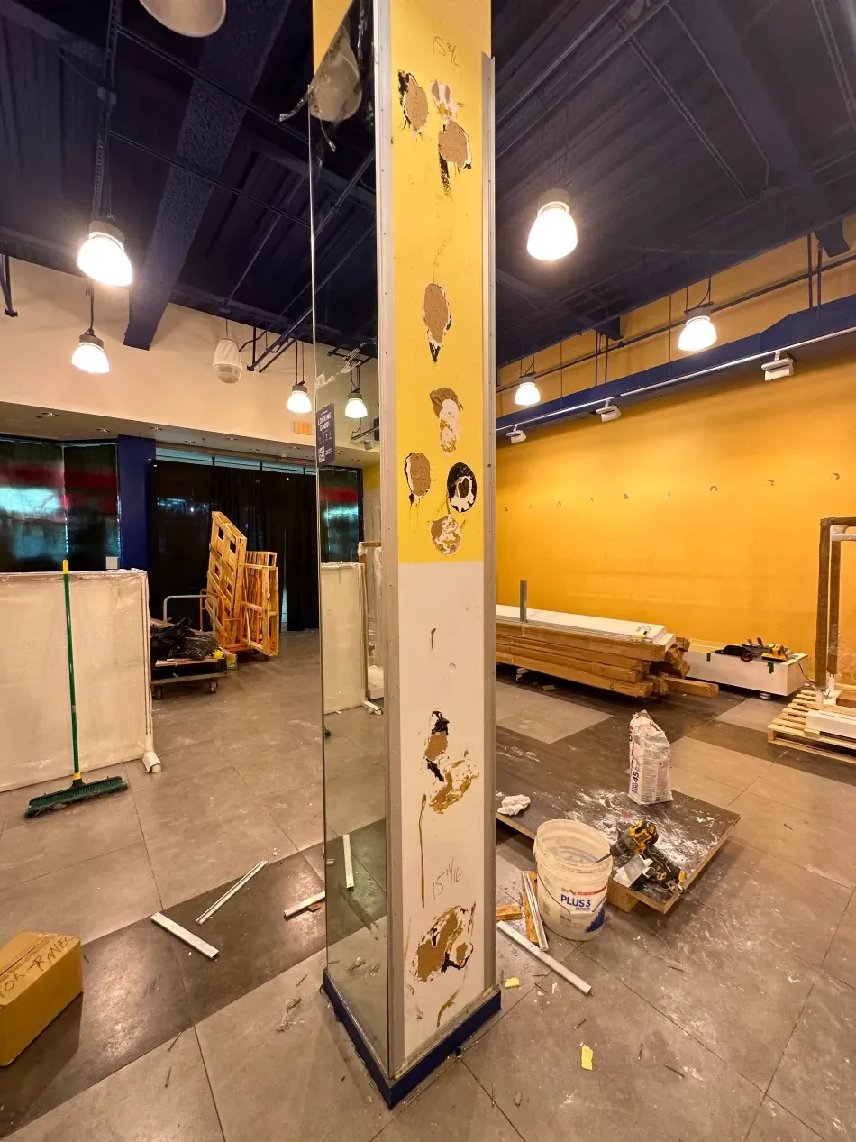 Interior of a retail space under construction. Yellow walls, blue ceiling, a central column with cartoon images, and scattered materials.