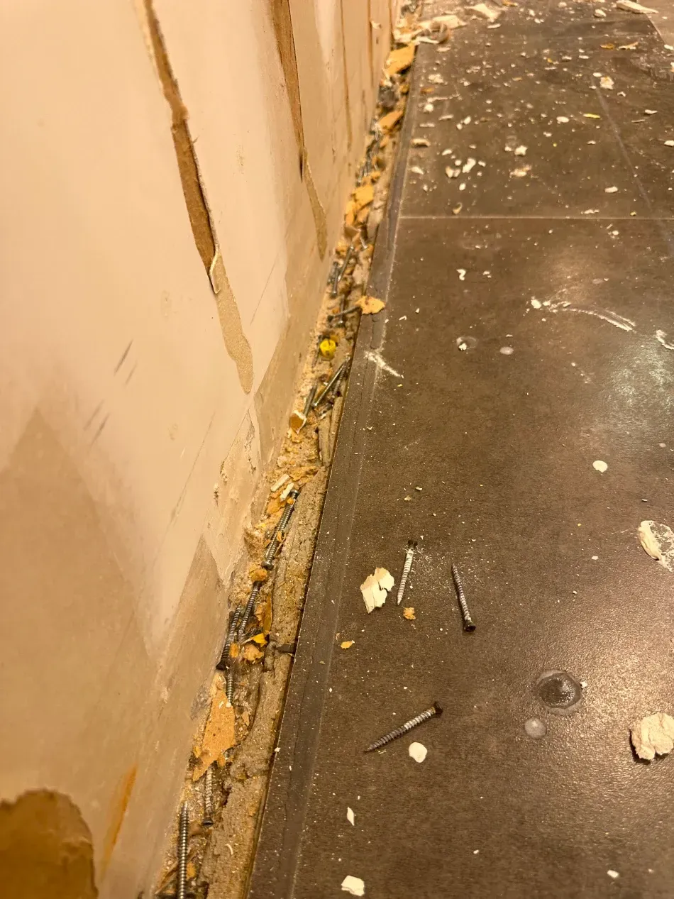 Wall baseboard removal in progress; debris on floor. Dark floor, light wall, exposed stud.