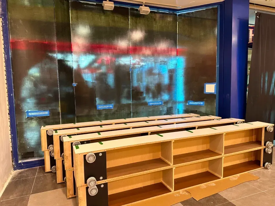 Empty wooden shelves in front of a dark, patterned wall. A blue corner column is on the right.