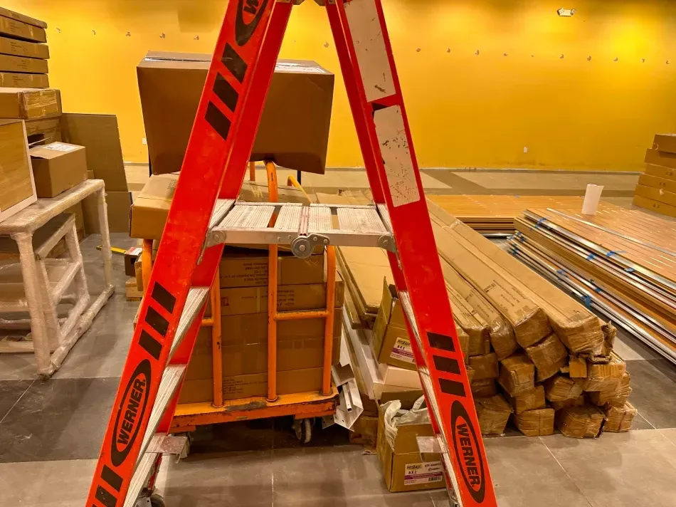 Red stepladder in front of a cart of boxes and other construction materials in a yellow-walled room.