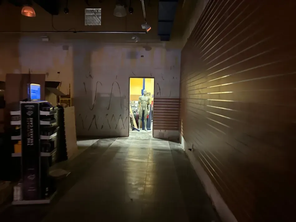 Dark hallway leads to open doorway with figures; product display on the left; brown paneled wall on the right.