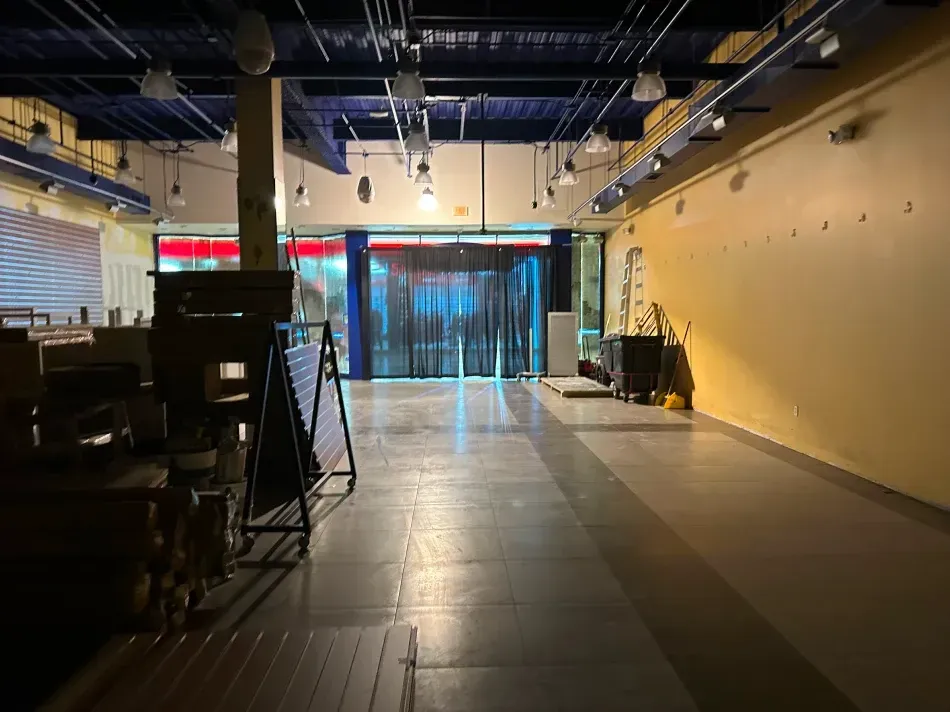 Empty commercial space with yellow walls, dark ceiling, and a doorway with dark curtains.