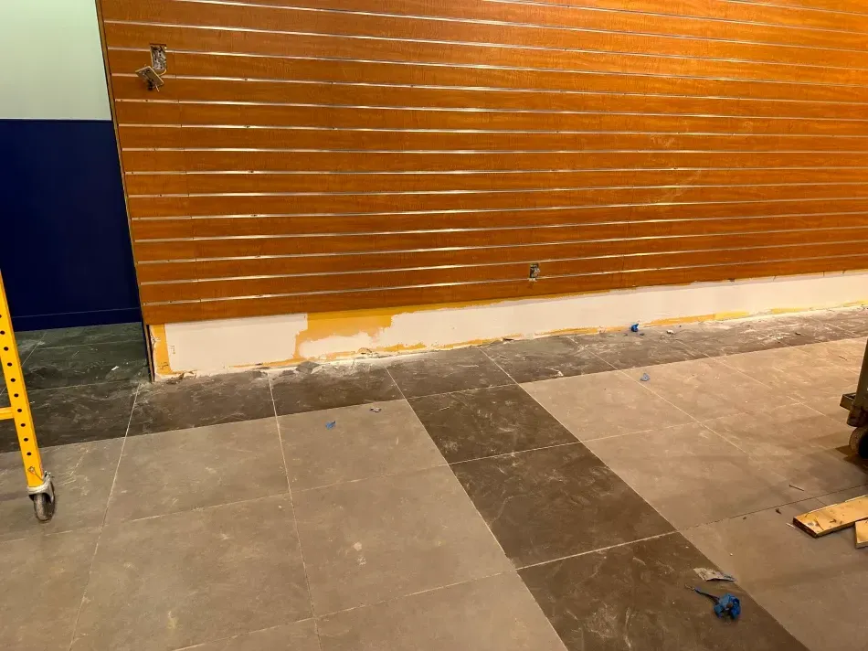 Wooden slatted wall above a tile floor, with exposed concrete. A blue wall and scaffolding are visible.
