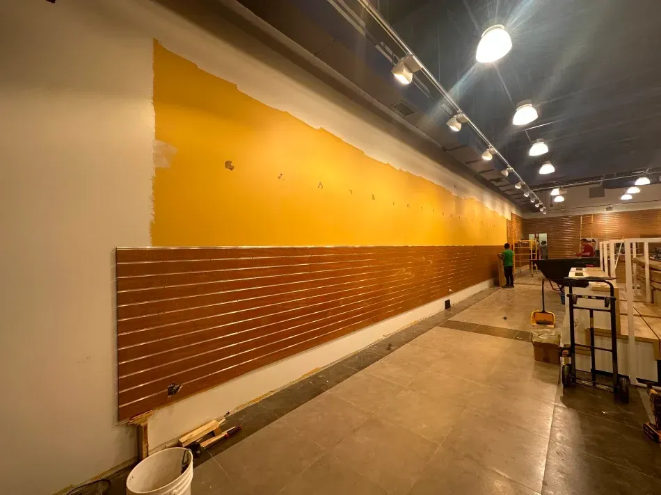 Interior renovation: Long wall with brown paneling, yellow paint, and construction worker.