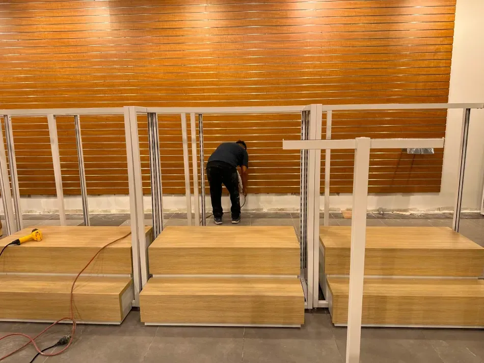 Person assembling display stands in front of a wood-paneled wall.