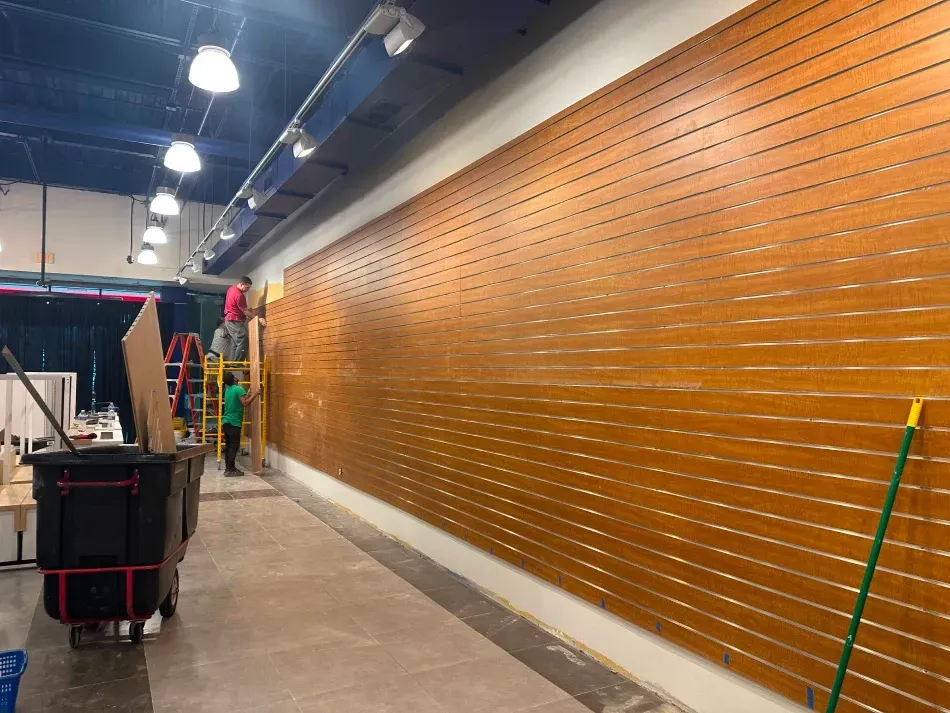 Workers installing wooden slat wall in a commercial space. A ladder is present.