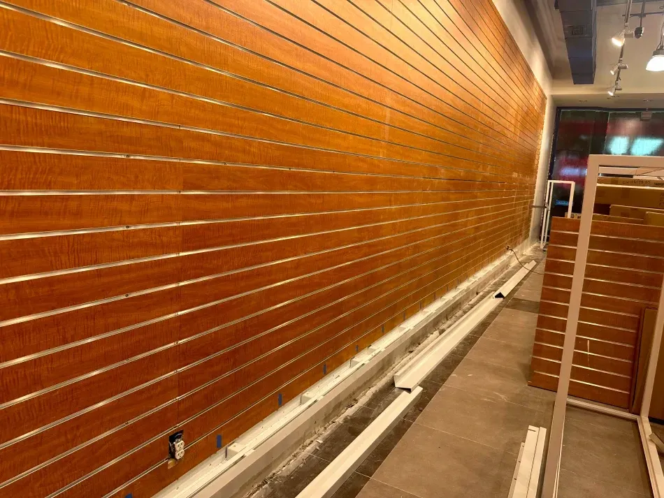 Wooden slat wall with metal grooves. White baseboards and support beams along the floor.