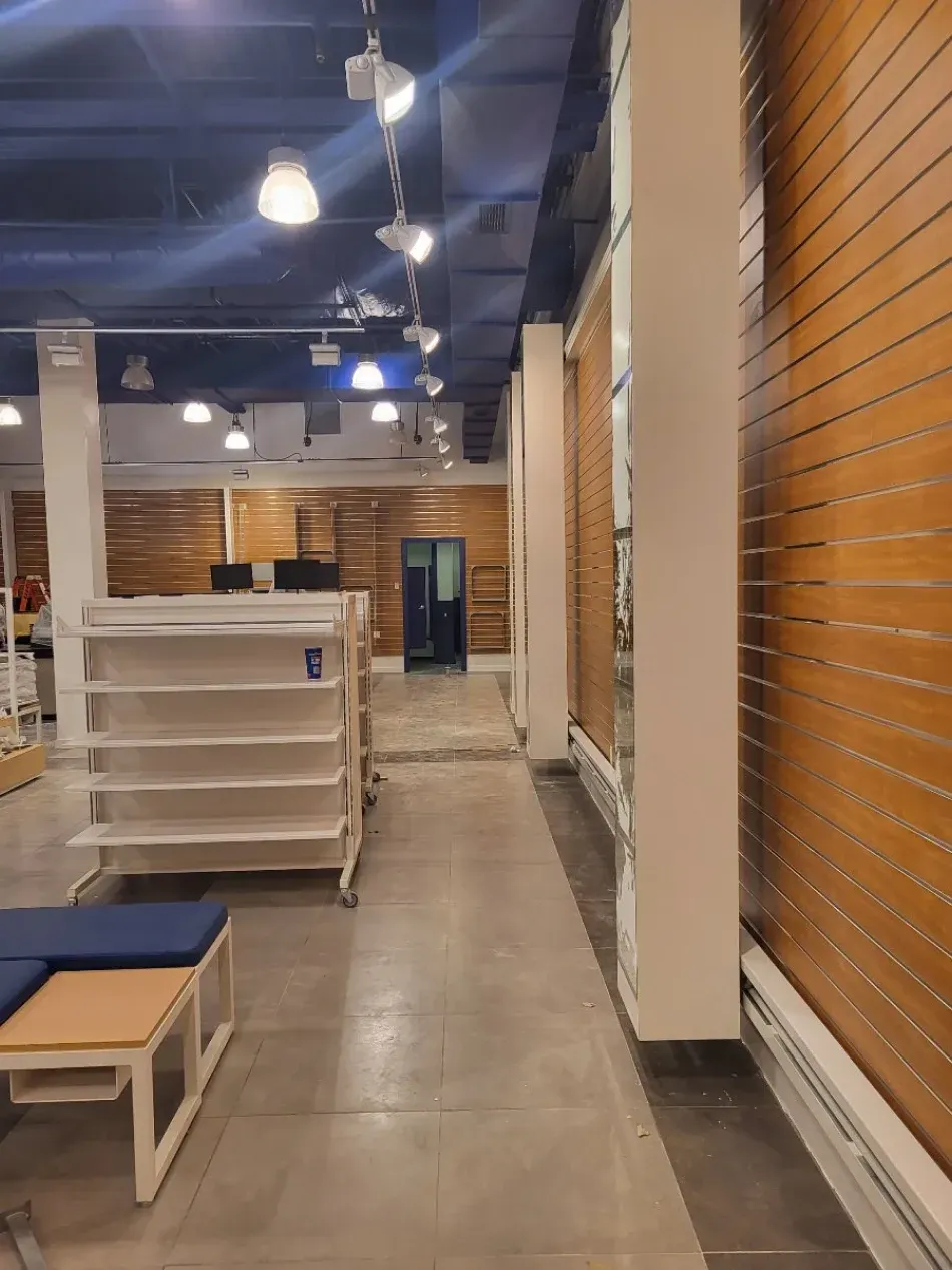 Empty retail store interior, wood paneling on walls, shelving units, blue door at the end of the aisle.
