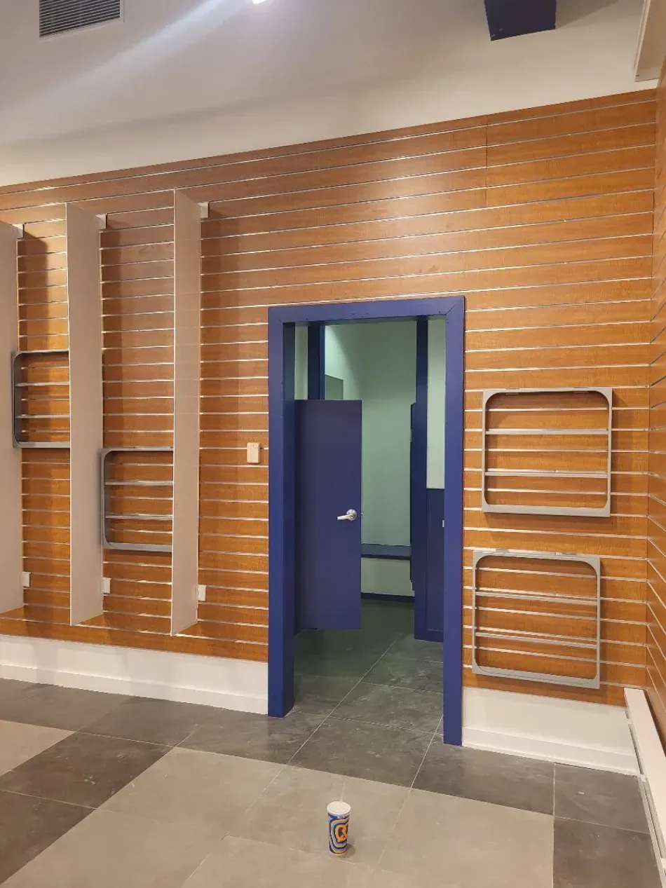 Interior with a blue door leading to a restroom. Wooden walls with shelves and a paint can on the floor.