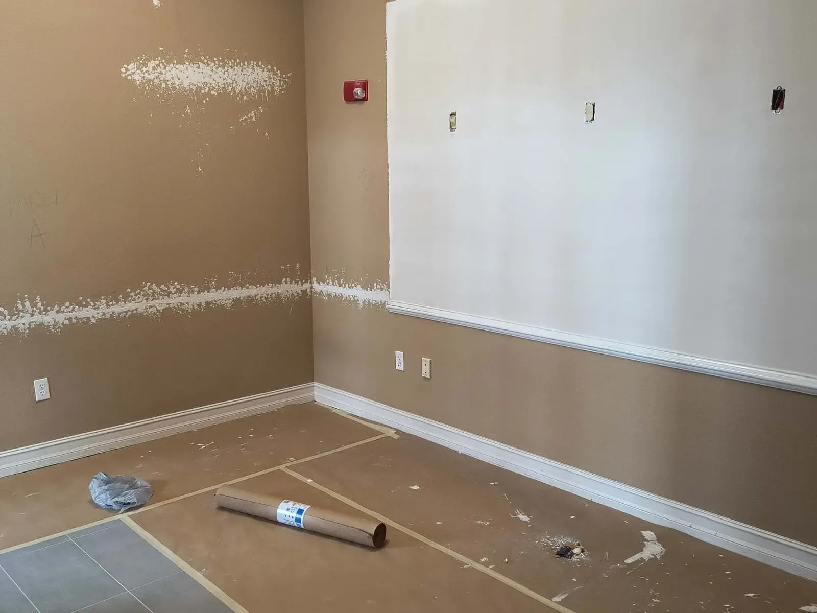 Room with unfinished paint job; tan walls, white trim and accents.
