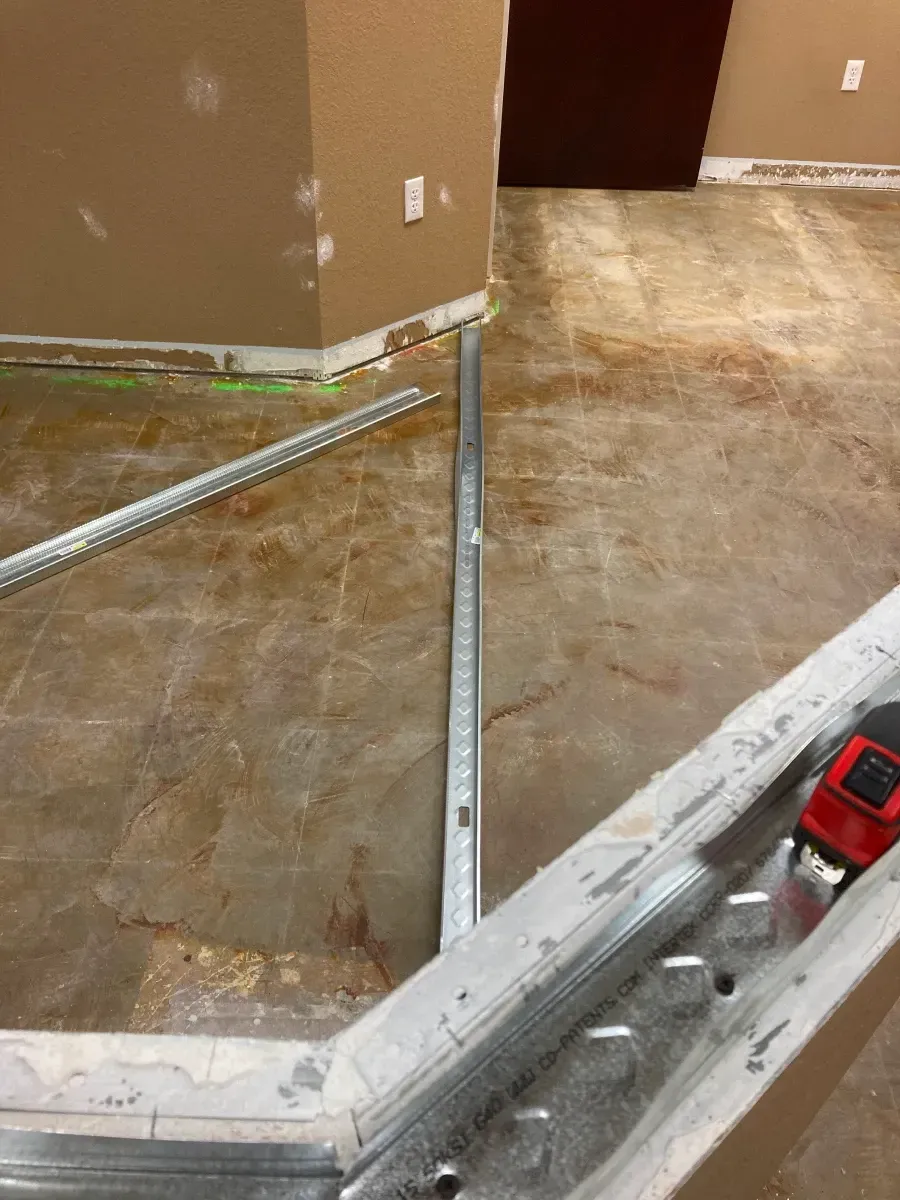 Metal studs on floor, forming a corner, in a room with tan walls and concrete floor.