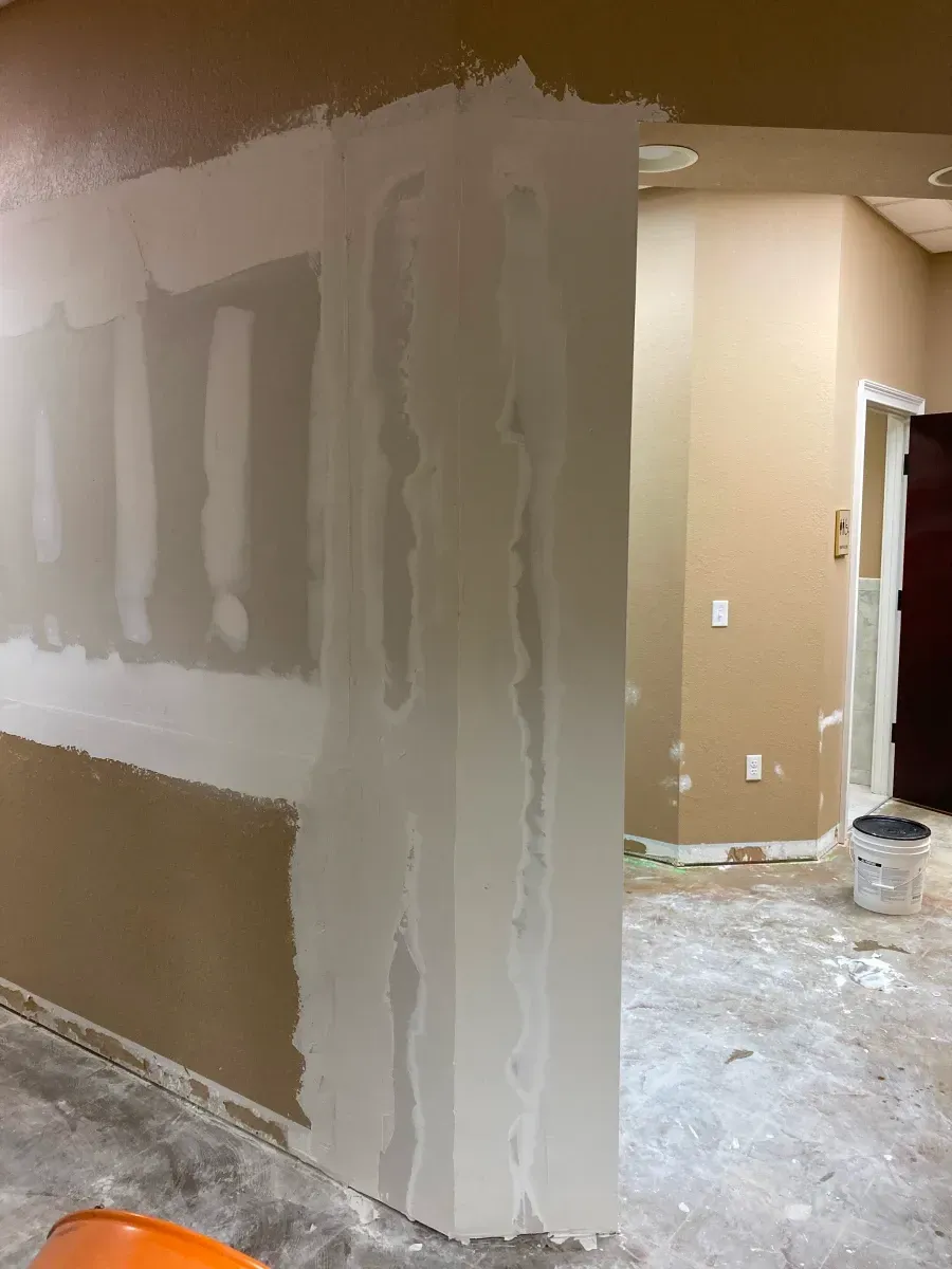 Drywall mudding on a wall, partially completed, with a doorway visible in a room under construction.