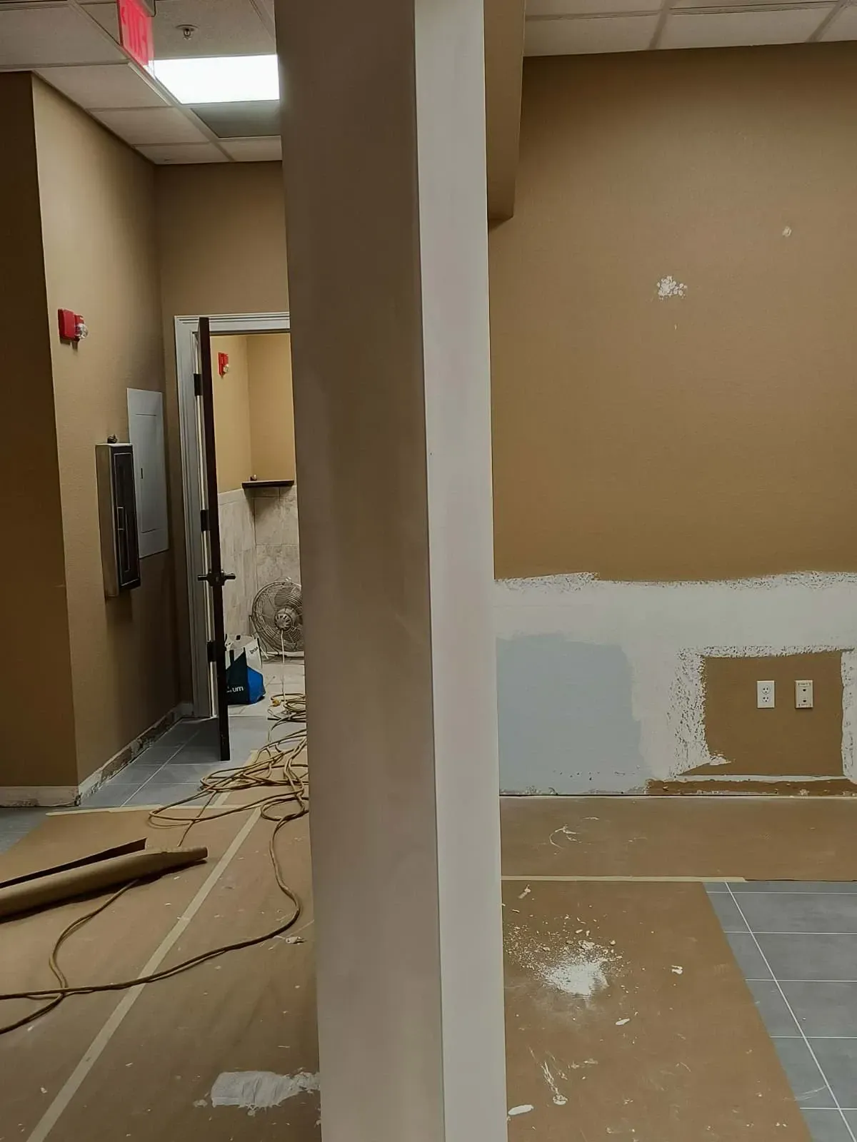 Interior view of a room under construction with a central support column. Brown and white walls, exposed wiring, and tools are visible.