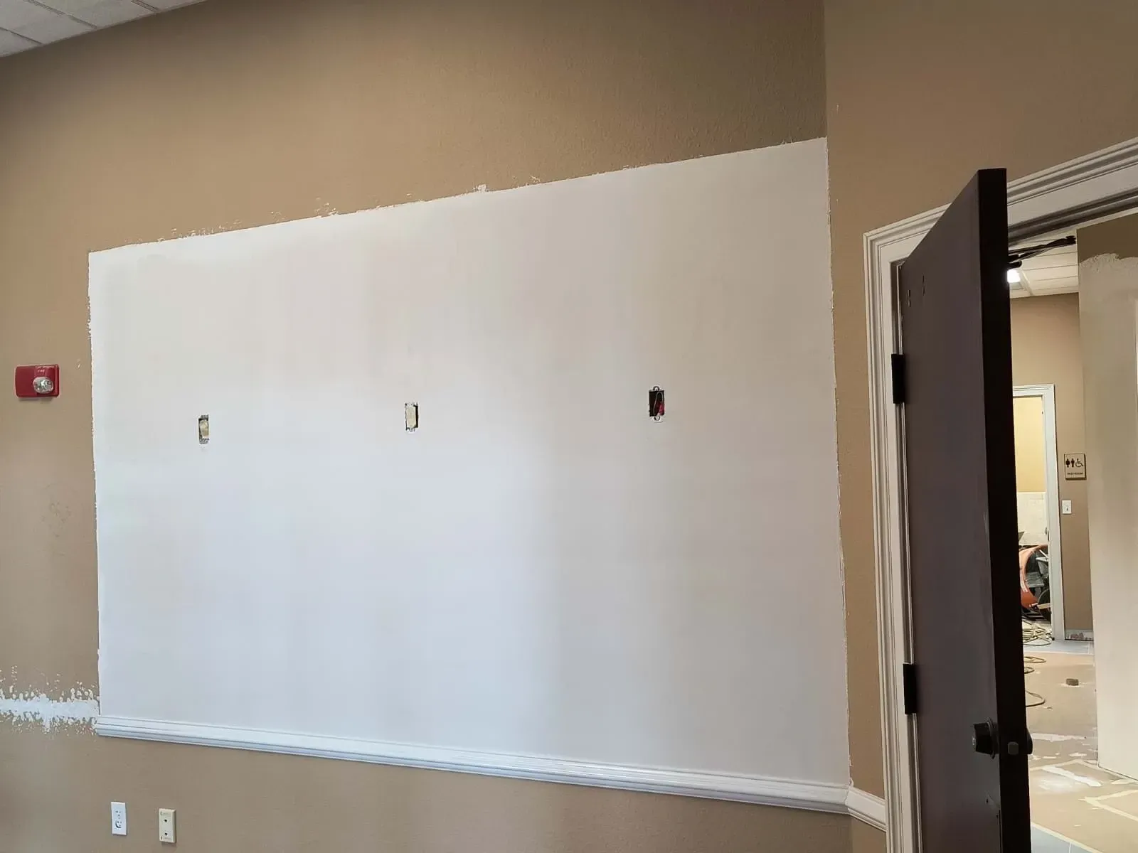 Large white painted section on a tan wall with three small holes. A dark door is open to the right.