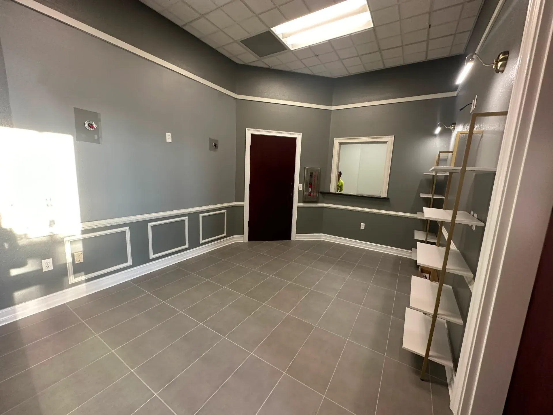 Empty gray room with tiled floor, dark door, window, and display shelving.