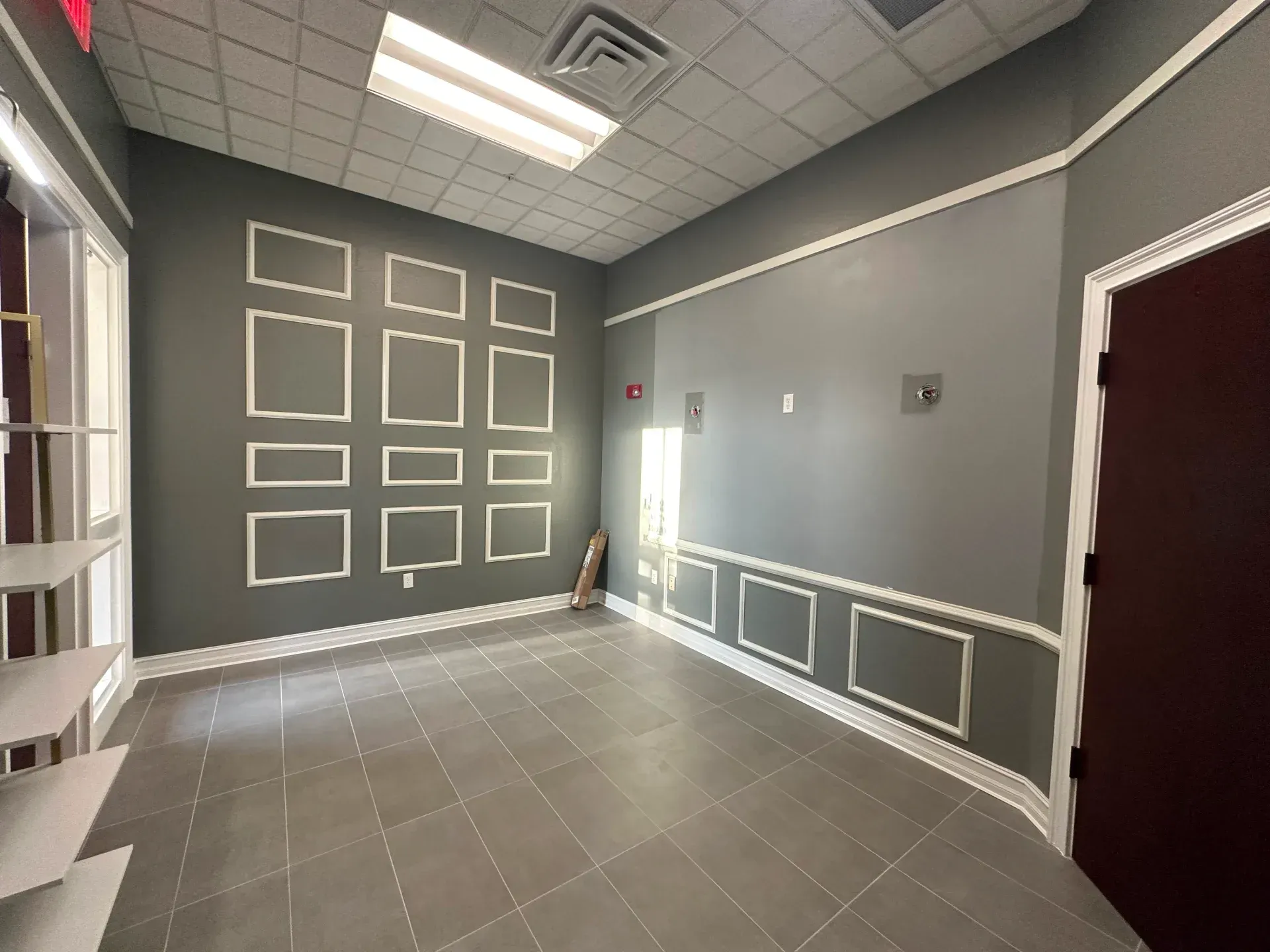 Empty room with gray walls, white trim, and a dark brown door. Floor tiles.