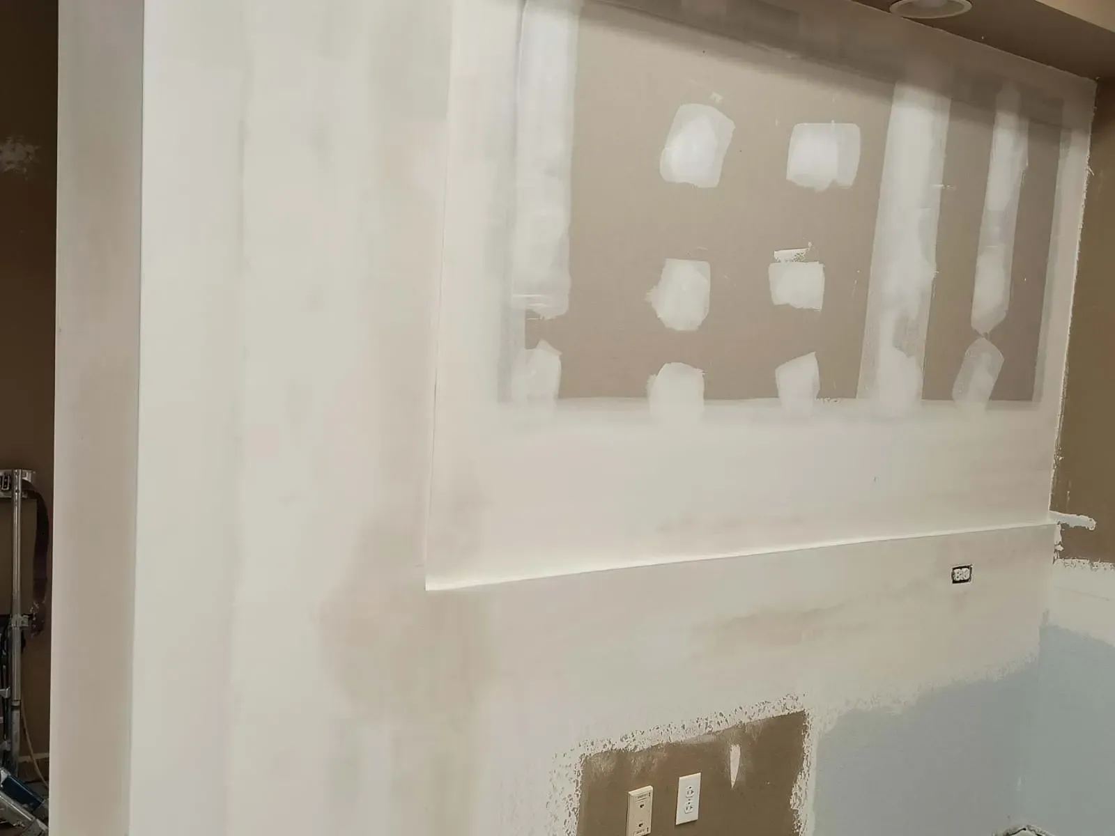 Drywall installation on a wall, white and tan colors, unfinished construction, light fixtures.