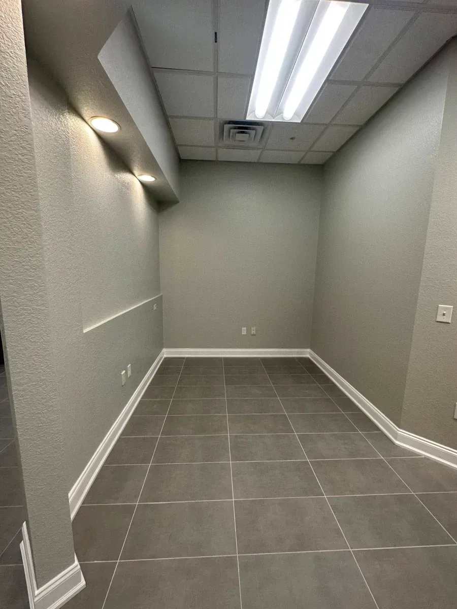 Empty office space with gray walls, tile floor, and fluorescent lighting.